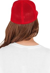 Căciulă roșie din plasă, cu partea din față structurată și boruri curbate, purtată peste părul lung și brunet, combinată cu un tricou alb.