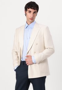 Double-breasted beige blazer with light blue shirt and dark pants. Blazer features a notched collar and two front pockets.