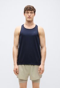 Μπλε σκούρο αμάνικο φανελάκι από ελαφρύ ύφασμα, με στρογγυλεμένο ντεκολτέ και πλευρικές σχισμές, σε συνδυασμό με μπεζ αθλητικό σορτς.