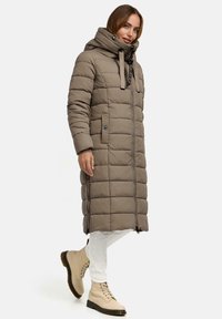 Lange, pufferjas in taupe met een hoge kraag en trekkoorden. Kenmerken zijn een gewatteerd patroon, zijzakken en een ritssluiting. Gekoppeld met beige laarzen.