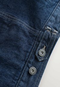 Sötétkék denim szövet, jól látható textúrával, a zsebénél díszvarrással és egy márkázott fém gombbal.