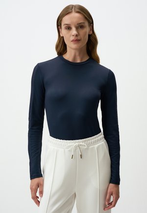 Marineblauw langemouwen top van gladde stof, slim fit design, en met gemusterde mesh accenten op de mouwen, gecombineerd met witte broeken met elastische taille.