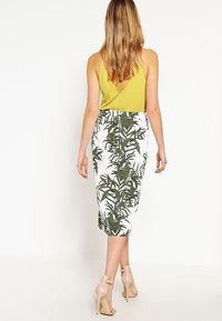 Grön och vit blommig pennkjol med en figurnära design; ihop med en ärmlös gul topp och beige klackar.