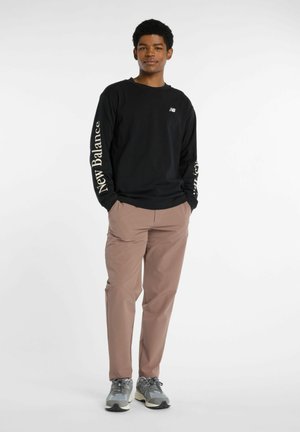 Black long-sleeve shirt with "New Balance" printed in white on sleeves, paired with light brown pants and gray athletic shoes.