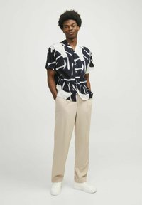 Camicia a maniche corte in bianco e nero con un audace motivo astratto, abbinata a pantaloni beige a gamba larga e sneakers bianche.