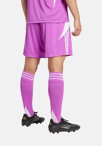 Roze voetbalshirt en -shorts met witte accenten, roze sokken met drie witte strepen, en zwarte voetbalschoenen met bronzen details.