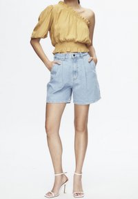 Top amarillo de un solo hombro con dobladillo fruncido combinado con shorts de mezclilla azul claro de talle alto, con bolsillos laterales y un ajuste relajado.