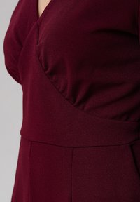Gros plan sur une robe bordeaux ajustée avec un bustier froncé et une ceinture large portée par une personne.