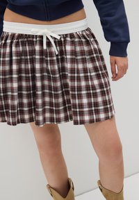 Gonna a quadri con una cintura elastica bianca e un dettaglio a fiocco, realizzata in tessuto leggero nei colori rosso, bianco e nero.