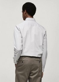 Cămașă cu dungi albe și gri, cu mâneci lungi și guler stil button-down, purtată împreună cu pantaloni maro deschis, care au două buzunare la spate.
