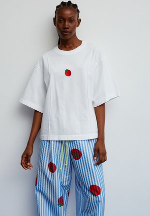 Camiseta blanca de algodón de manga corta con un pequeño bordado de tomate rojo en el pecho, combinada con pantalones azules de rayas que presentan patrones de tomate rojo.