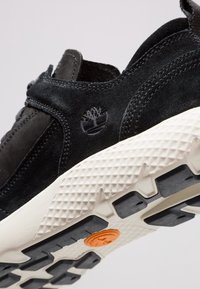 Svart mocka sneakers med en texturerad vit och svart gummisula. Har en subtil präglad logotyp och elastiska detaljer för en säker passform.