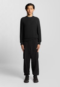 Maglione nero con scollatura rotonda, abbinato a pantaloni cargo neri larghi. Il tessuto appare morbido, con una finitura texturizzata e tasche pratiche.