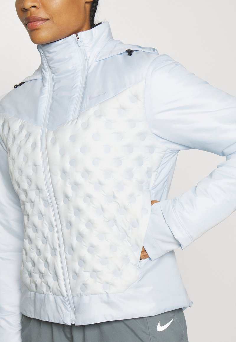 Hellblaues Jacket mit einer gepolsterten, strukturierten weißen Vorderseite mit kreisförmigen Mustern, hohem Kragen und seitlichen Taschen mit Reißverschluss.
