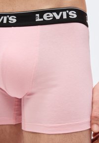 Κοντινό πλάνο ενός ατόμου που φοράει ροζ εσώρουχα μπόξερ Levi's με μαύρη ελαστική μέση που φέρει το λογότυπο Levi's.