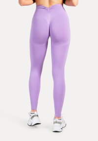 Leggings viola a vita alta con fascia in vita texturizzata, design aderente e finitura senza cuciture, abbinati a scarpe da ginnastica bianche.