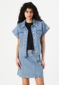 Jachetă din denim cu mâneci scurte, de culoare albastru deschis, cu nasturi în față și două buzunare pe piept; asortată cu o fustă din denim de aceeași culoare.