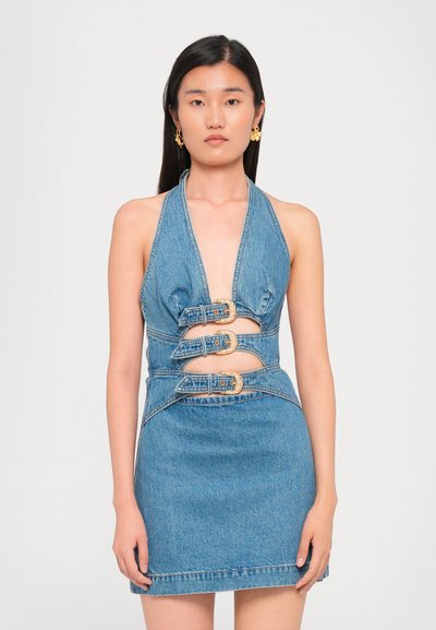 Denimkjole med halterneck, tætsiddende design, tre guldspænder og en kort længde. Naturlig blå farve med en let struktureret overflade.