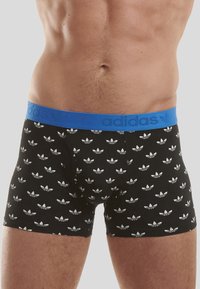 Boxers noirs avec des motifs blancs de logo adidas, dotés d'une ceinture élastique bleue embossée du nom de la marque. Le matériau semble doux.