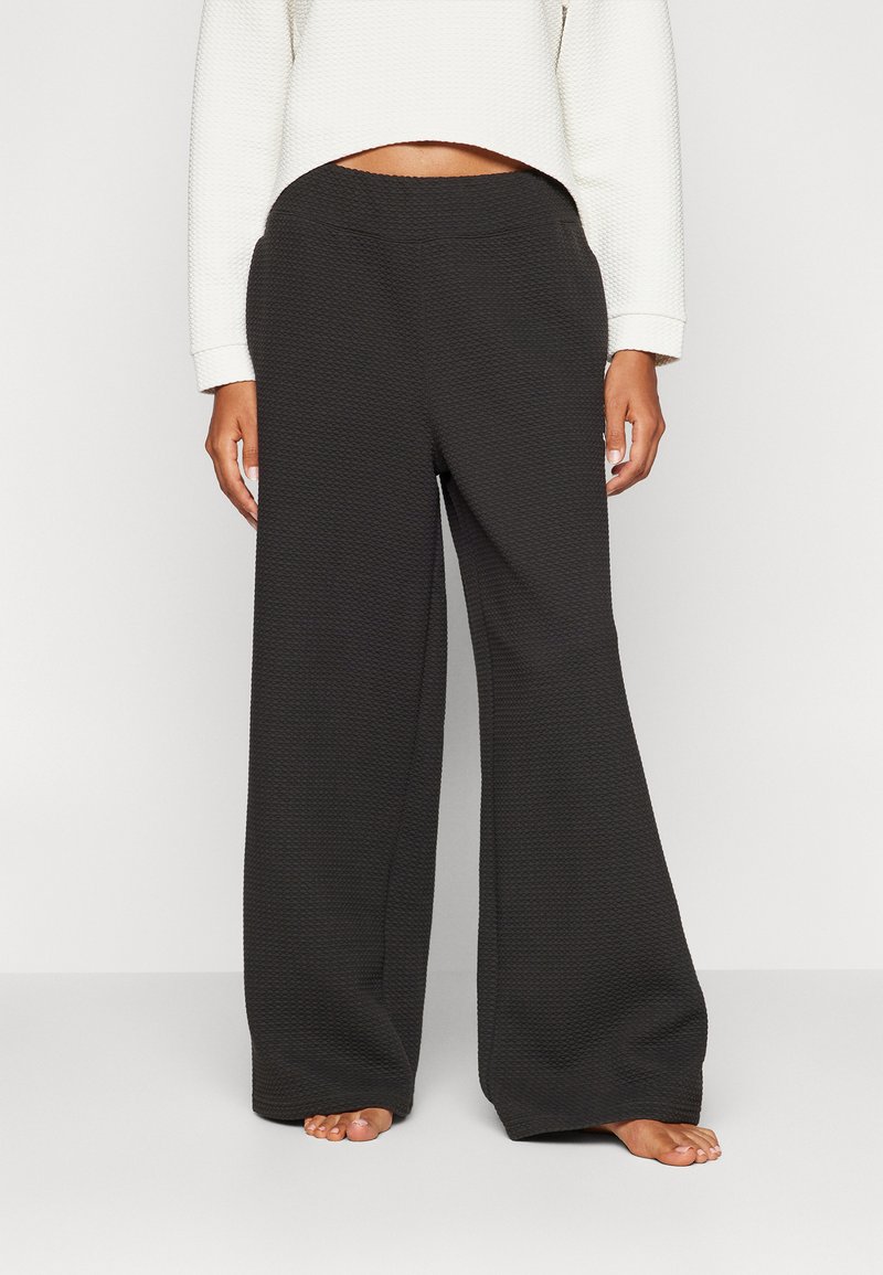 Pantalones negros de pierna ancha hechos de una tela texturizada, con una cinturilla simple y un corte holgado. El diseño se extiende hasta los tobillos.