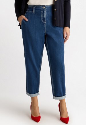 Dunkelblaue Denim-Hosen mit einem lässigen Schnitt, hochgekrempelten Säumen, Fronttaschen und einem Knopfverschluss. Kombiniert mit roten Absatzschuhen.