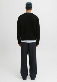 Schwarzer Strickpullover mit lockerer Passform und rundem Ausschnitt. Kombiniert mit weit geschnittenen, vertikal gestreiften Hosen in dunklen Farbtönen.