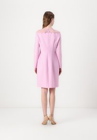 Vestido rosa con mangas largas, corsé ajustado, escote con forma de ondas y una cremallera en la parte posterior. Tejido suave y estructurado. Diseño hasta la rodilla.