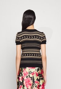 Svart stickad topp med korta ärmar och geometriska mönster i krämfärg och brunt. Fitted form med ribbade ärmsluten och halsringning.