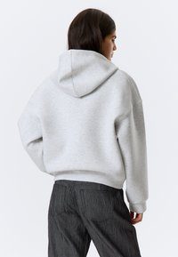 Grijze hoodie met een relaxte pasvorm, zachte textuur en oversized silhouet, gecombineerd met zwarte gestructureerde broek.