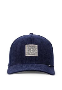 Gorra de pana azul marino con visera plana, que presenta un parche bordado cuadrado en la parte frontal con detalles de diseño intrincados.