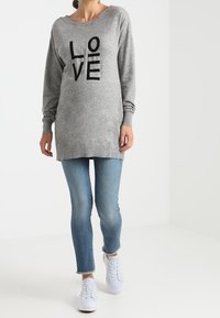 Šedý svetr s černým textem "LOVE", dlouhé rukávy, kulatý výstřih. V kombinaci s světle modrými skinny džíny a bílými teniskami.