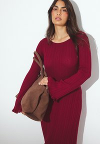 Gestreiftes, langärmliges Kleid in tiefrot, getragen mit einer braunen Wildleder-Schultertasche. Die Tasche hat einen Reißverschluss und eine weiche Textur.