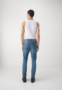 Světle modré džíny s přiléhavým střihem, se zadními kapsami a koženou nášivkou na pasu, nošeny s bílým tílkem.