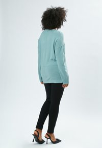 Maglione oversize in verde chiaro con maniche lunghe, lavorato a maglia testurizzata, abbinato a leggings neri e tacchi aperti neri.