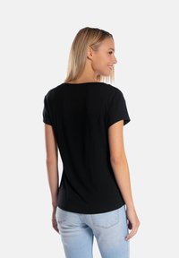 Czarny krótki T-shirt z okrągłym dekoltem, wykonany z miękkiej tkaniny. Posiada luźny krój oraz lekko zaokrąglony dół.