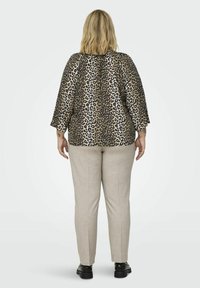 Leopardenmuster-Oberteil mit lässiger Passform und weiten Ärmeln, kombiniert mit hellbeigen Hosen. Die Schuhe sind schwarz mit glänzender Oberfläche.