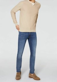Pull en tricot beige avec col rond, associé à un jean en denim bleu slim. La chaussure est composée de mocassins en daim marron clair.
