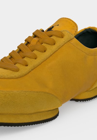 Baskets en suède jaune avec lacets assortis et logo noir brodé sur la languette, dotées d'une semelle texturée et d'un embout arrondi.