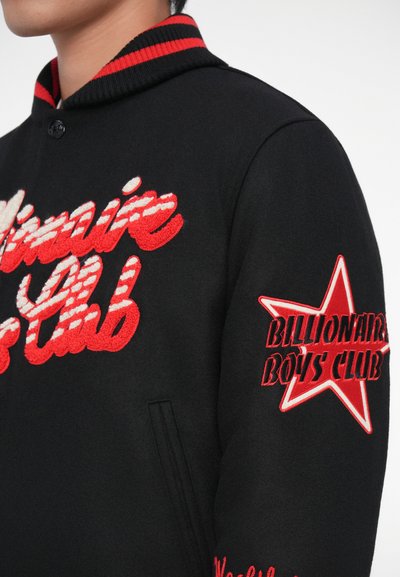 Casaco varsity de lã preto com letras bordadas em vermelho e branco; apresenta um colarinho canelado e detalhe de estrela na manga.