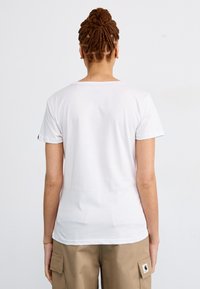 T-shirt en coton blanc à manches courtes, encolure ronde et texture lisse. Porté avec un pantalon cargo beige avec des détails de poche.