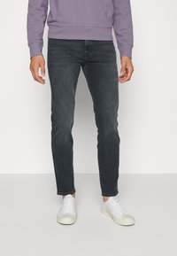 Jeans di denim blu scuro con vestibilità slim e leggero effetto slavato. Abbinati a sneakers bianche e a una felpa lilla chiaro.