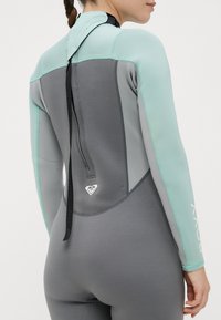 Sērfošanas neoprēna kostīms pelēkā un zilo krāsā, ar augstu apkakli, garām piedurknēm un rāvējslēdzēja aizdari aizmugurē, ar zīmola marķējumu apakšā.