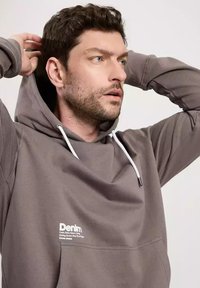 Szara bluza z kapturem, przednia kieszeń i białe sznurki. Posiada małe białe logo na obszarze klatki piersiowej. Gładka faktura materiału.