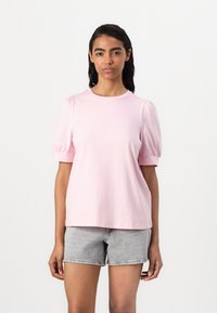 Ljust rosa blus med puffärmar i mjukt tyg, med rund halsringning och avslappnad passform, matchad med gråa denimshorts.