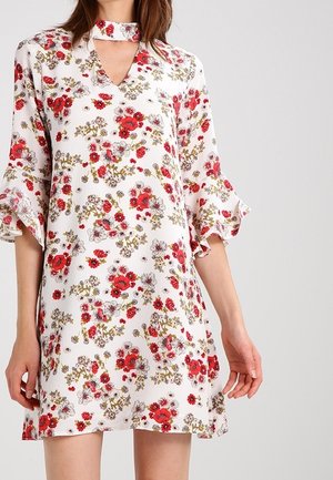 Witte bloemenjurk met rode en groene bloemen, gerimpelde mouwen tot aan de elleboog en een V-hals met een choker-achtige kraag.