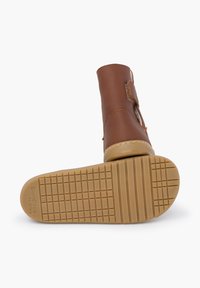 Hnědá kožená kotníková bota s prošitými detaily, suchým zipem a texturovanou gumovou podrážkou se vzorem mřížky.