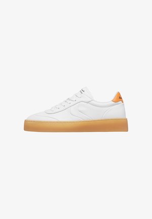 White low-top sneaker with gum sole and orange heel tab, featuring lace-up closure and subtle wave-shaped side detail.