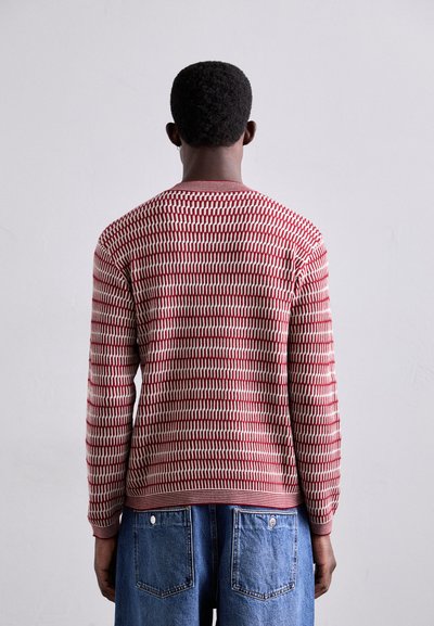 Pull tricoté à motifs rouge et blanc avec des manches longues, un col rond et un tissu texturé, associé à un short en jean bleu.