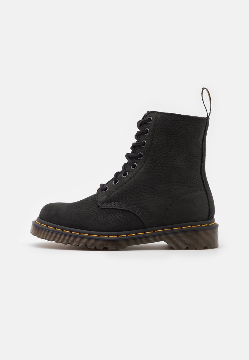 Bottine noire en cuir à lacets avec détail de coutures jaunes, semelle épaisse à rainures, et languette à l'arrière sur fond blanc.