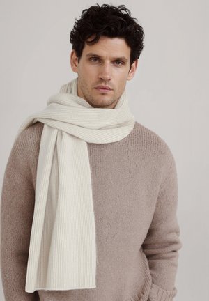 Écharpe crème côtelée en tissu doux enroulée autour d'un pull en maille beige. L'écharpe présente une texture lisse et des bords nets.